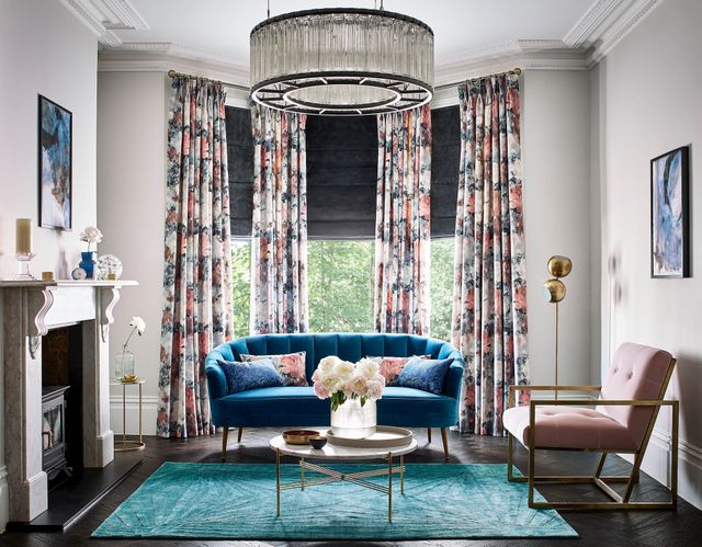 Dark grey velvet roman blind under floral print curtains in a bright living room with blue and rose pink accents