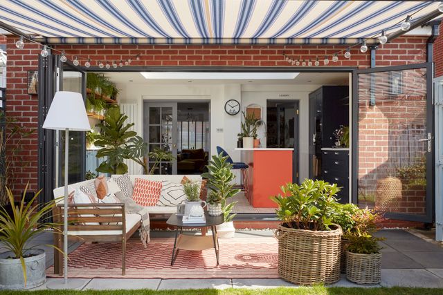 a white and blue striped awning fitted above a door window with chairs and table under it