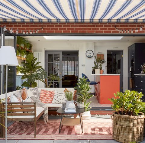 Blue and white awning in a garden with a sofa, coffee table, free standing lamp and rug