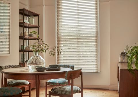 Natural Bamboo Seashell blind in a dining room with shelves on the left and a circular table with chairs to the left side and a cabinet on the right. 