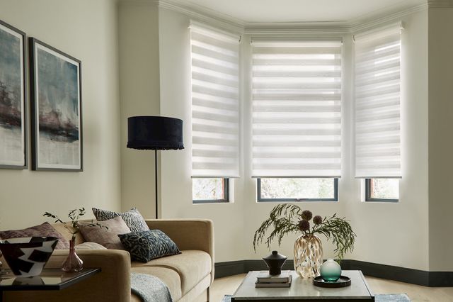 daybreak white day and night blind in a bay window in a living room with a sofa, table and lamp