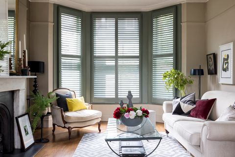 dark green full height shutters in a living room two white sofas glass table and black fire place surrounded by cream walls