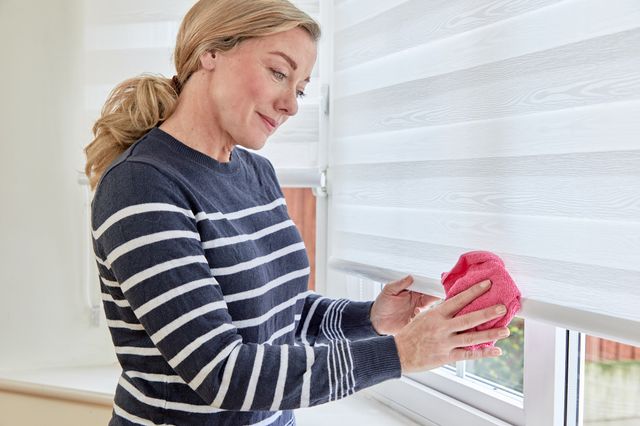 woman cleaning white day & night roller blinds with red cloth