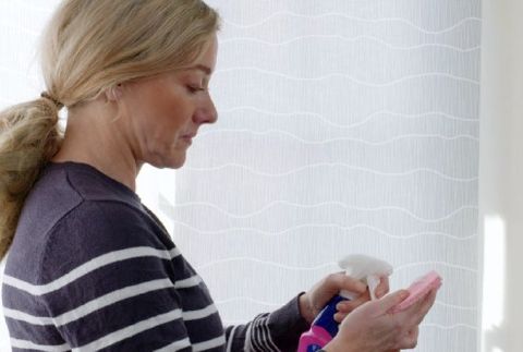 lady with blonde hair using cleaner spray on a sponge ready to clean roller blind