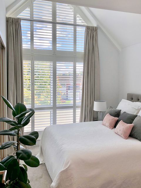 long full height shutters on huge window with triangular shutters on the top in bedroom
