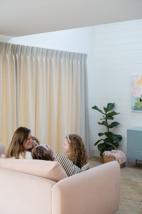 A-family-sitting-on-a-pink-couch-in-a-living-room-with-pencil-pleat-curtains