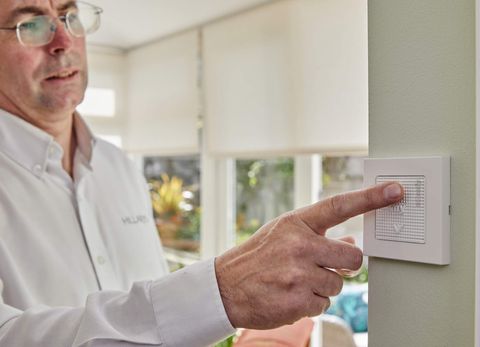 A male Hillarys adviser pushes the wall switch that controls the roller blinds behind him in a conservatory.